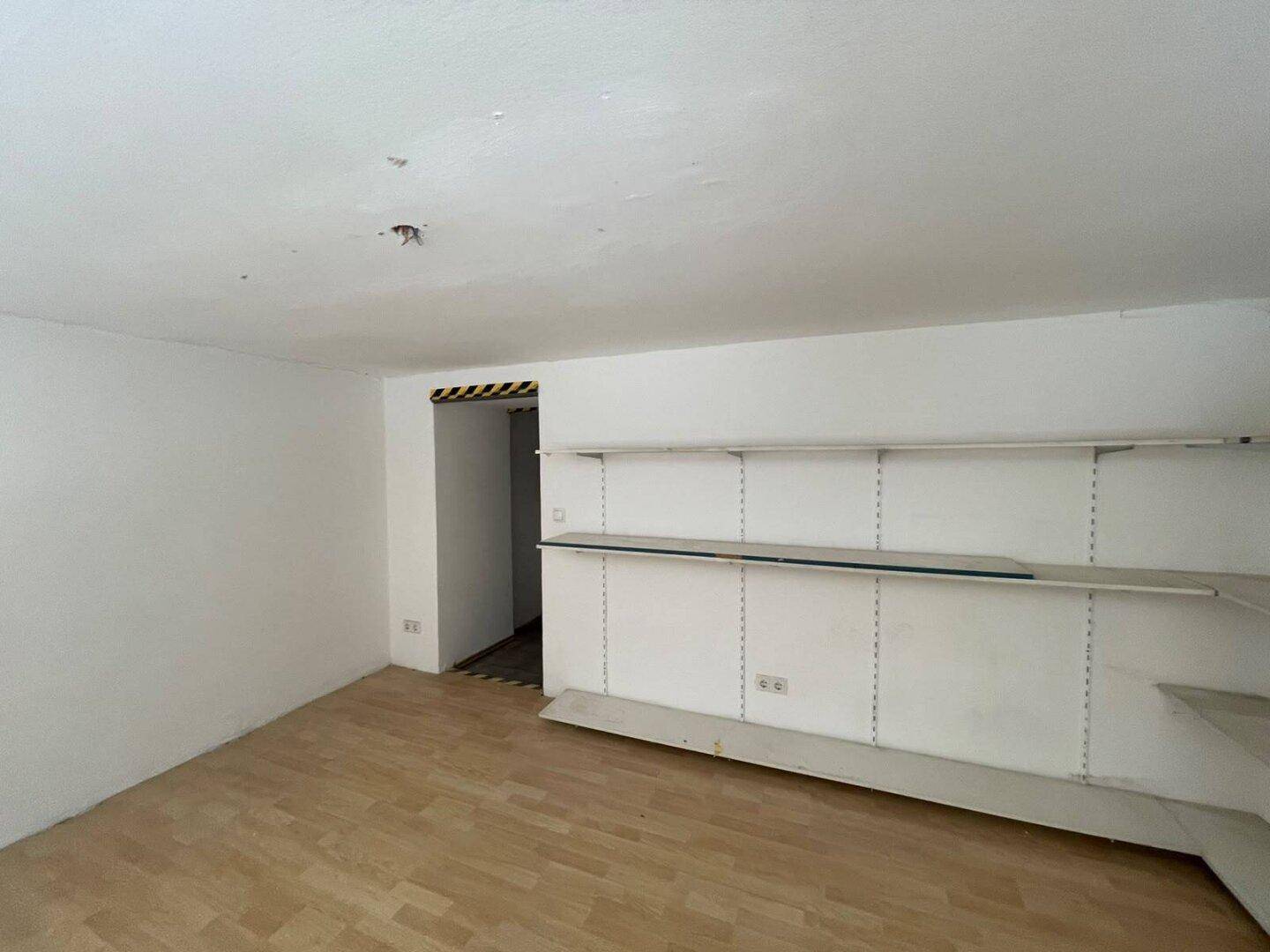 Hinterer Bereich eines Ladenlokals mit Regalsystemen und Holzboden, ideal für Lagerung oder Präsentation.
