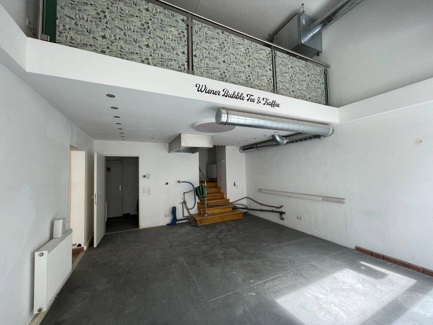 Kommerzieller Raum mit Betonboden, sichtbaren Lüftungsrohren und einer Galerieebene, die eine offene Atmosphäre schafft.