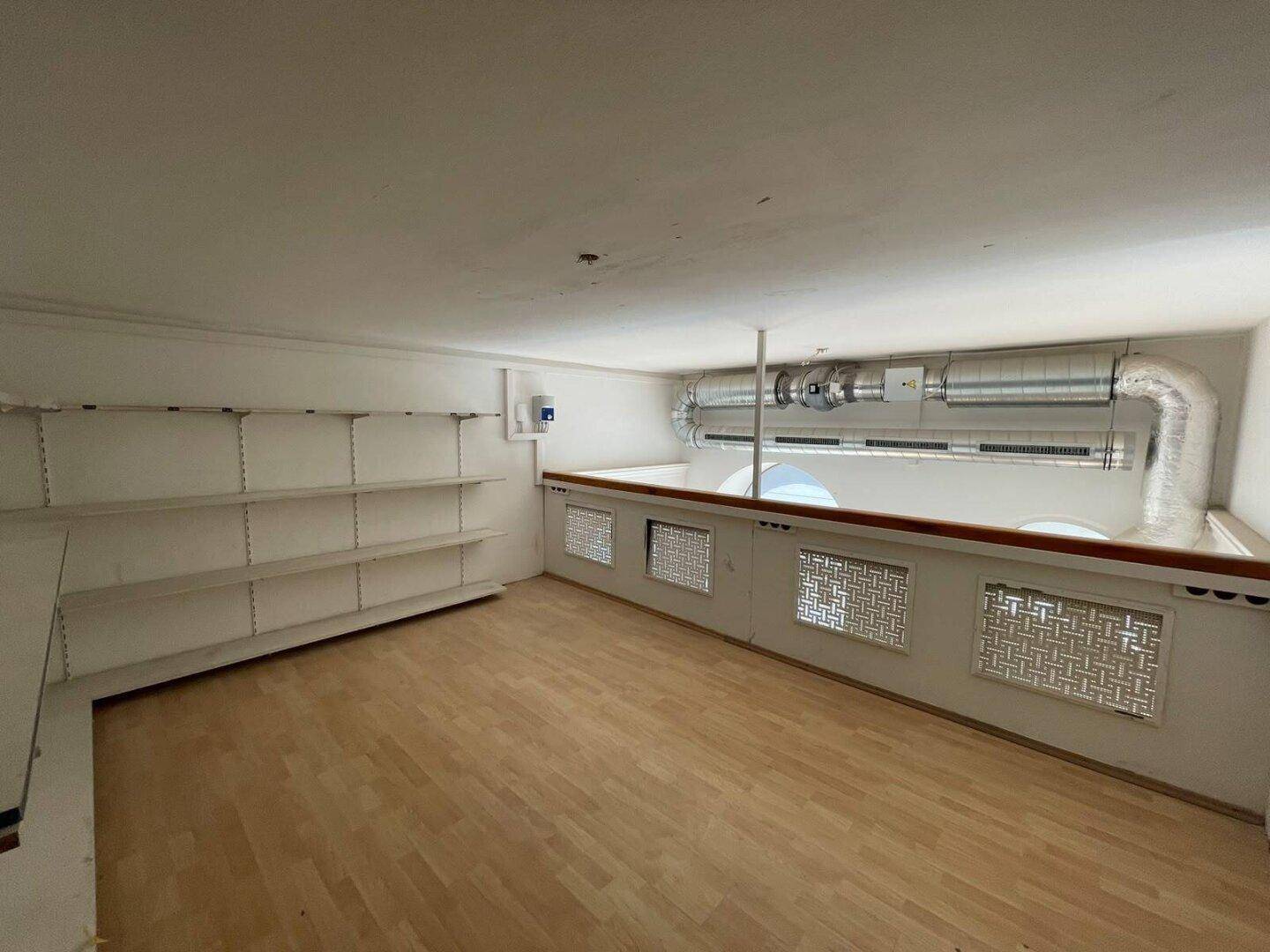 Galeriebereich mit Regalen, Holzboden und sichtbaren Lüftungsrohren, die den Raum funktional gestalten.