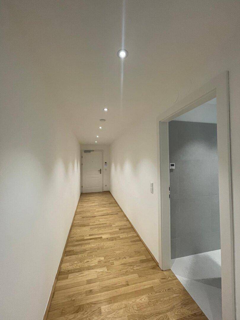 Heller Flur mit Holzboden und modernen Einbaustrahlern, der zu den Zimmern führt.