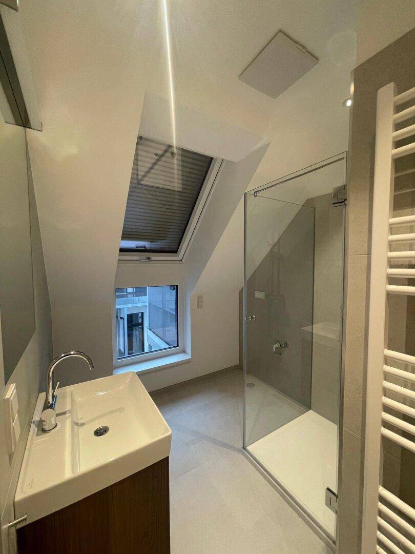 Modernes Badezimmer mit Dusche, Einzelwaschbecken und Dachfenster für natürliches Licht.