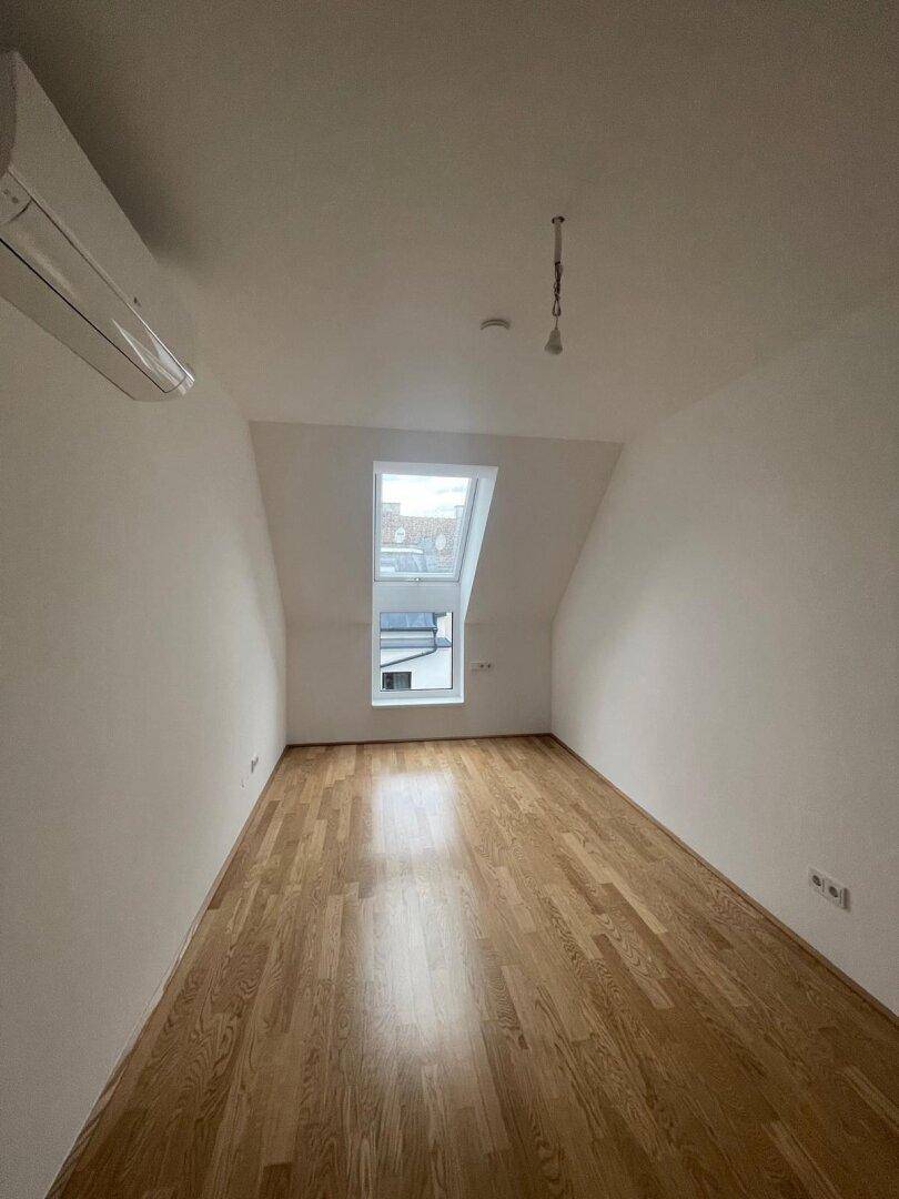 Geräumiges Dachzimmer mit Holzboden, Dachfenster und installierter Klimaanlage.