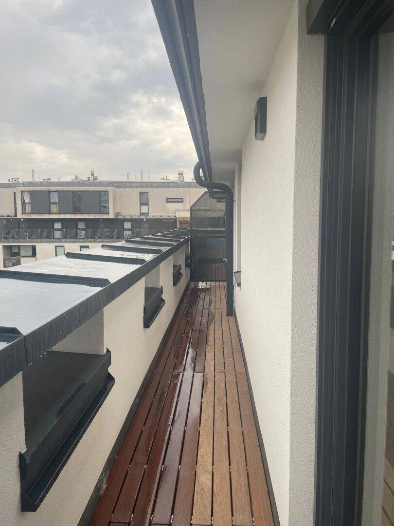Langer, schmaler Balkon mit Holzdielen und Blick auf die städtische Umgebung.