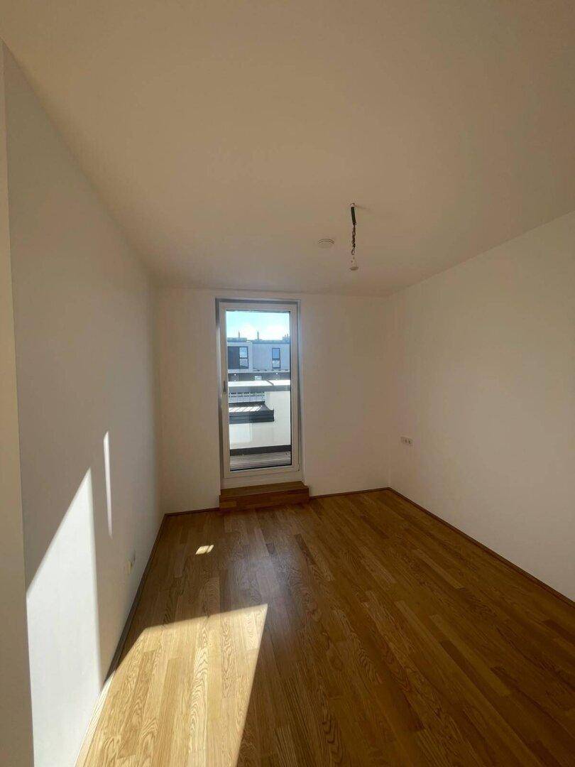 Helles Zimmer mit Parkettboden und Zugang zu einem Außenbereich, ideal als Schlaf- oder Arbeitszimmer.