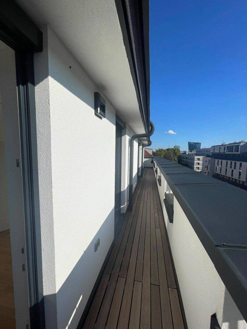 Langer, schmaler Balkon mit Holzbelag und Blick auf die umliegenden Gebäude.