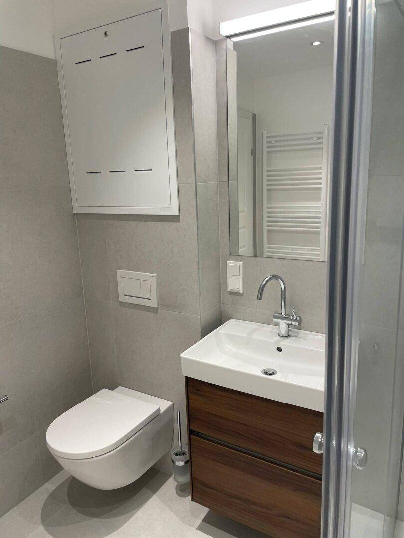 Modernes Badezimmer mit grauen Fliesen, wandhängendem WC, Einzelwaschbecken und Duschkabine.