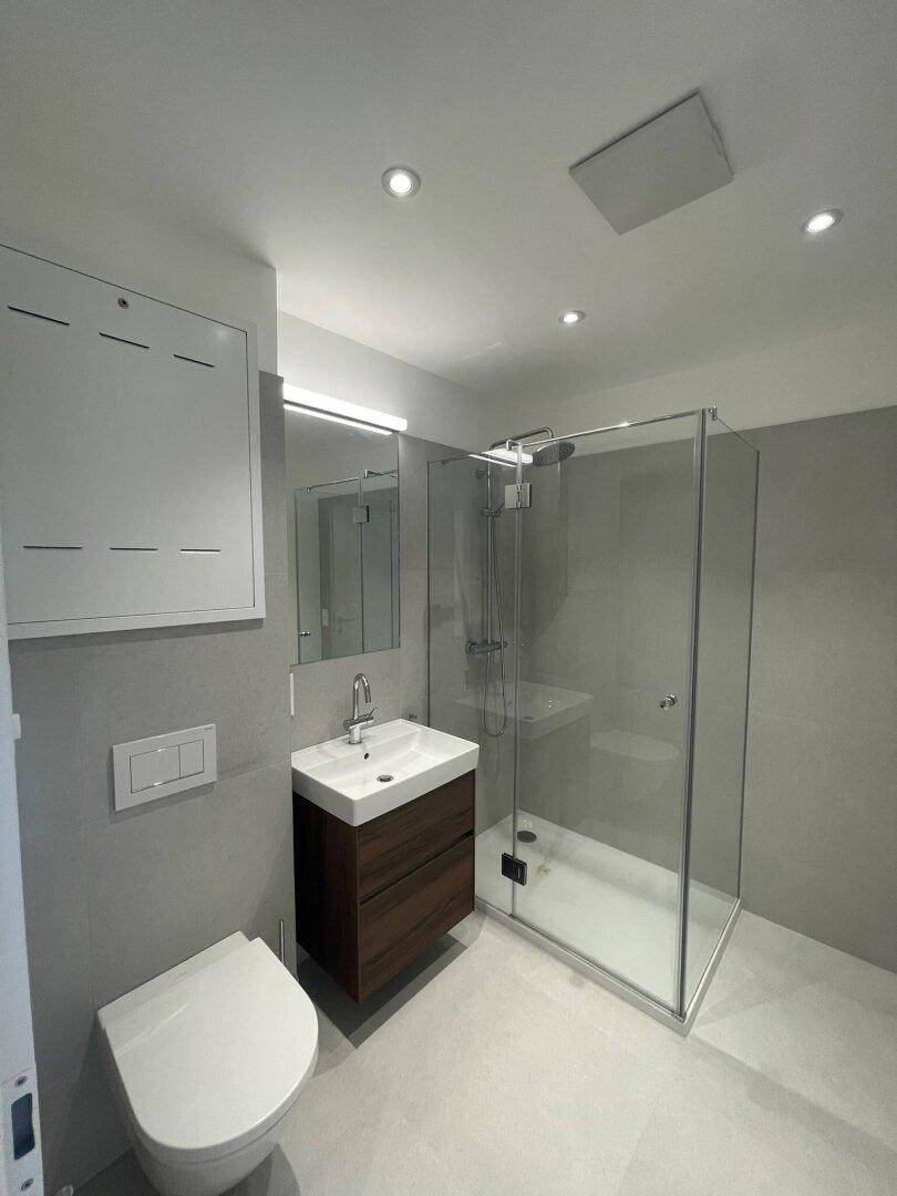 Helles Badezimmer mit modernen grauen Fliesen, wandhängendem WC und einer geräumigen Duschkabine.