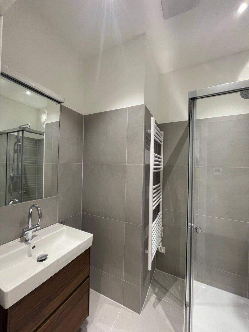 Modernes Badezimmer mit grauen Fliesen, Waschtisch, Duschkabine und beheiztem Handtuchhalter.