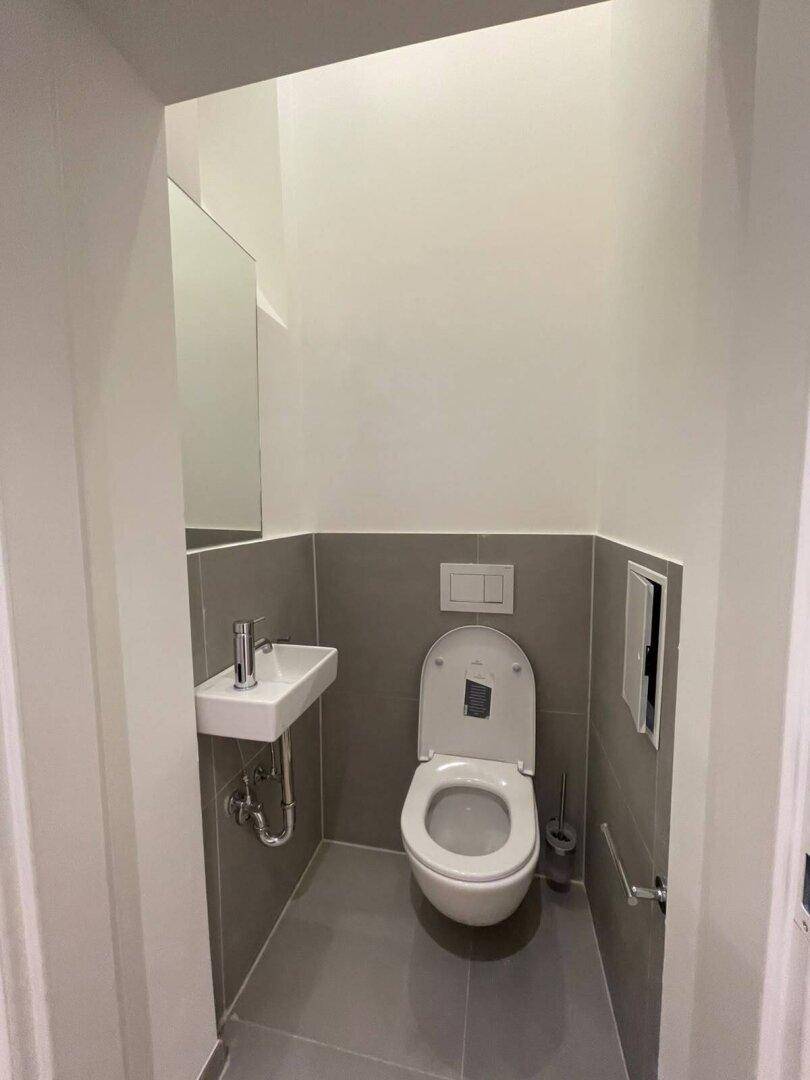 Separates Gäste-WC mit modernen grauen Fliesen, wandhängendem WC und kleinem Handwaschbecken.