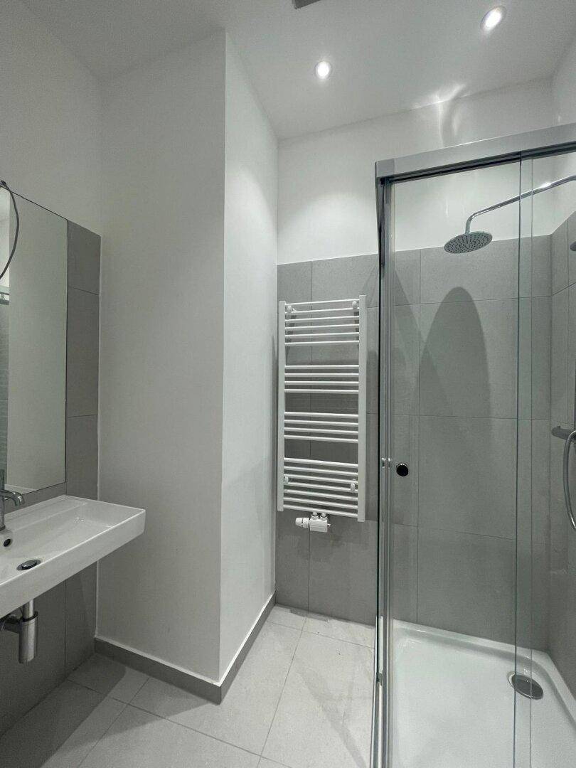 Zeitgemäßes Badezimmer mit Duschkabine, beheiztem Handtuchhalter und grauen Wandfliesen.