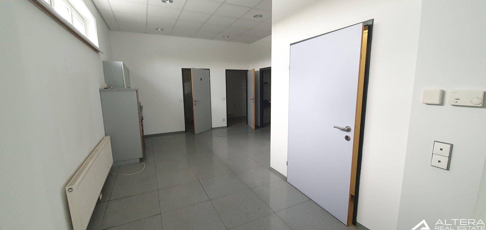 Heller Raum mit Fliesenboden und mehreren Türen, der als Büro oder Gemeinschaftsbereich genutzt werden könnte.