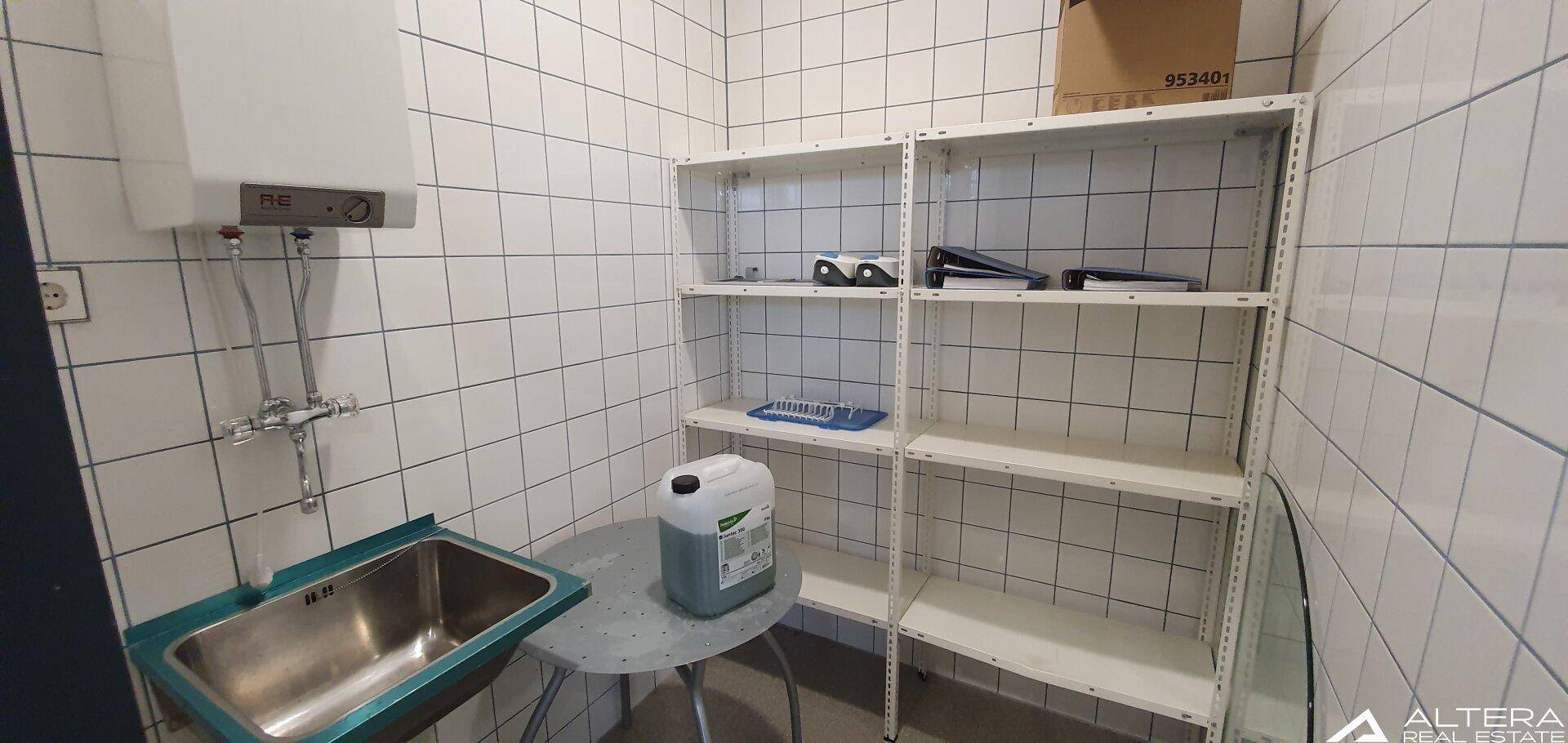 Kleiner Abstellraum mit gefliesten Wänden, Waschbecken und Regalen, ideal für Lagerung und Reinigung.
