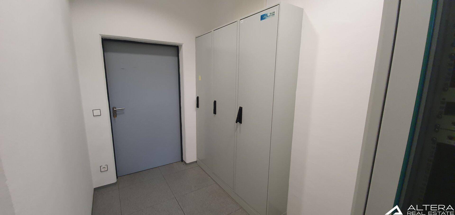 Kleiner Raum mit grauen Aktenschränken und einer Tür, ideal für Lagerung oder Archiv.
