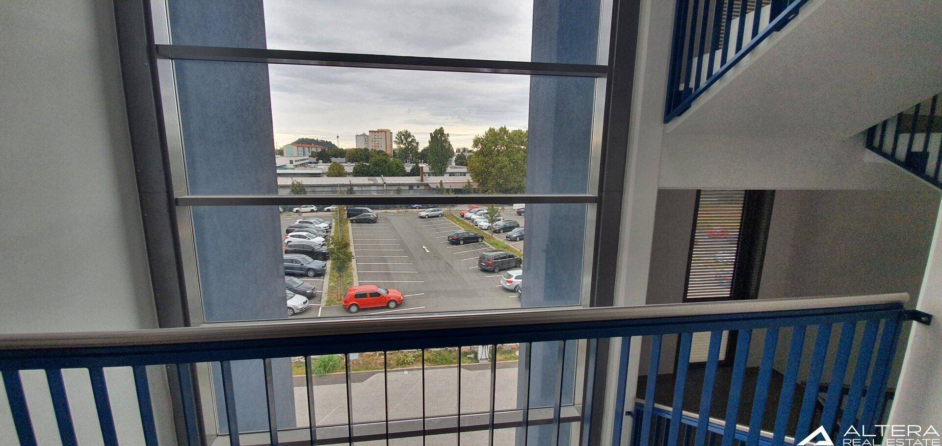 Treppenhaus mit großen Fenstern, die einen Blick auf einen Parkplatz und die Umgebung bieten.
