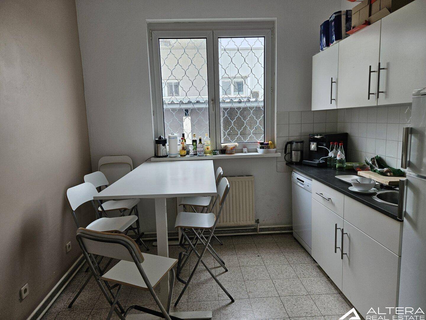 Kleine Küche mit weißer Einbauküche, Esstisch und Fenster mit Blick auf die Umgebung.