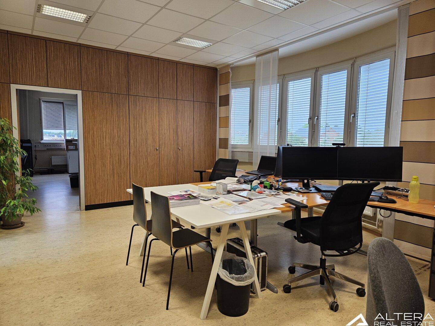 Büro mit Holzvertäfelung, Besprechungstisch und mehreren Arbeitsplätzen mit Blick nach draußen.