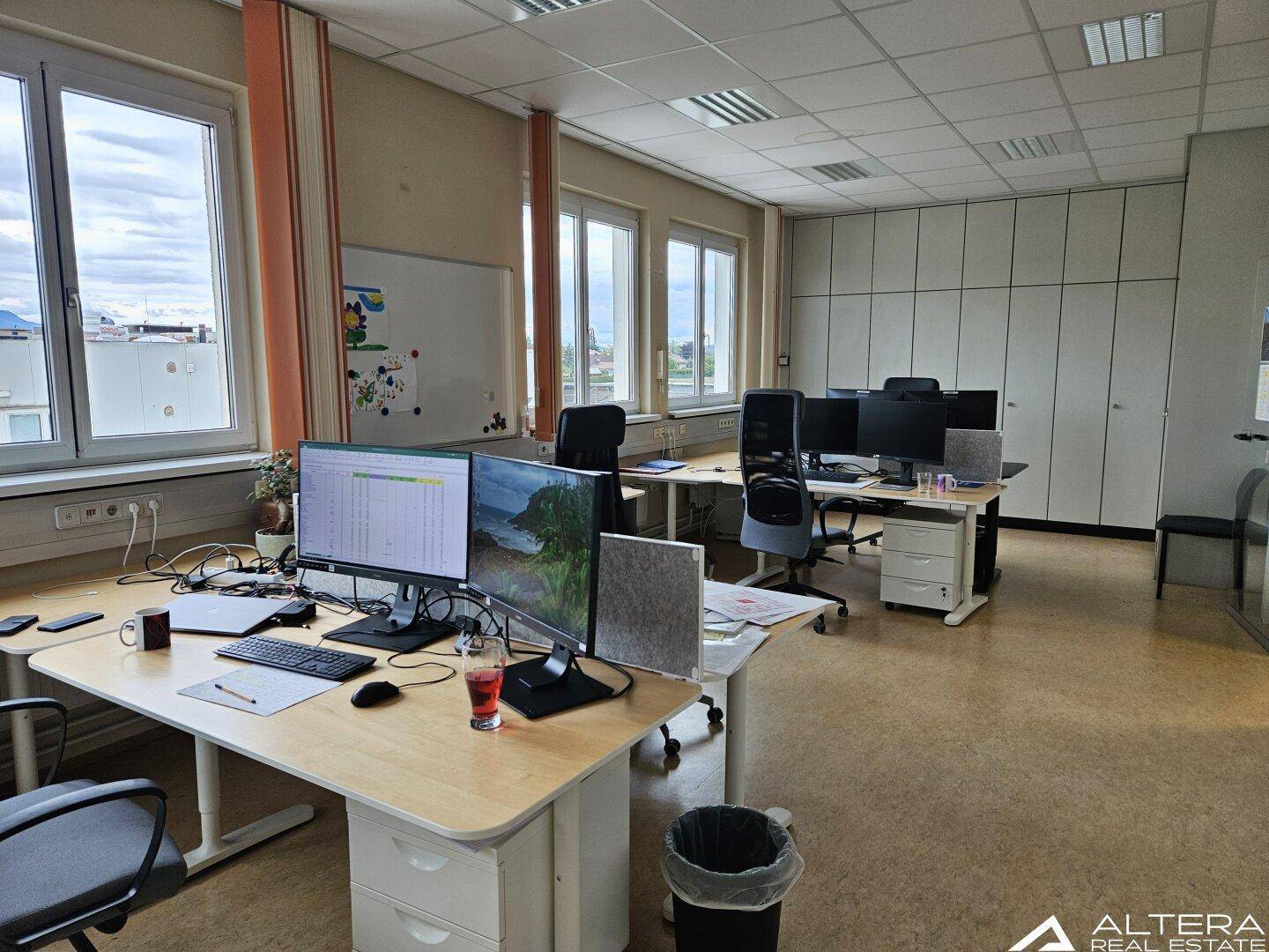 Helles Büro mit mehreren Arbeitsplätzen, großen Fenstern und Blick auf die Umgebung.