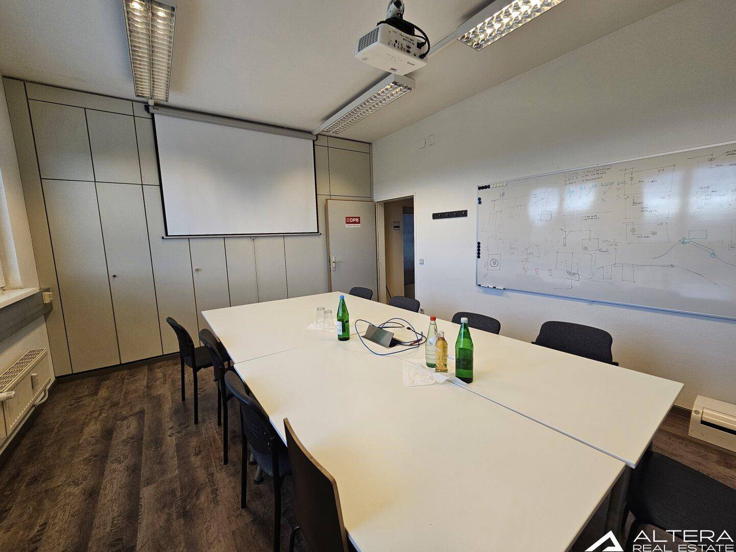Geräumiger Konferenzraum mit großem Tisch, Beamer und Projektionsfläche für Präsentationen.