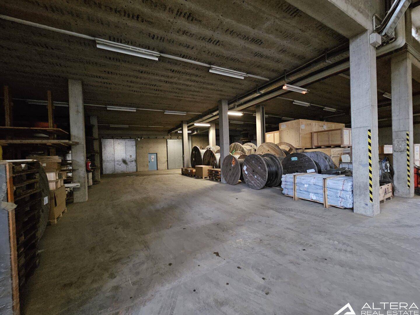 Geräumige Lagerhalle mit Betonboden, hohen Decken und gelagerten Kabelrollen und Kisten.