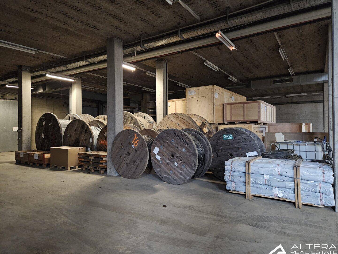 Lagerbereich mit Betonboden, hohen Decken und großen Kabelrollen sowie verpackten Gütern.