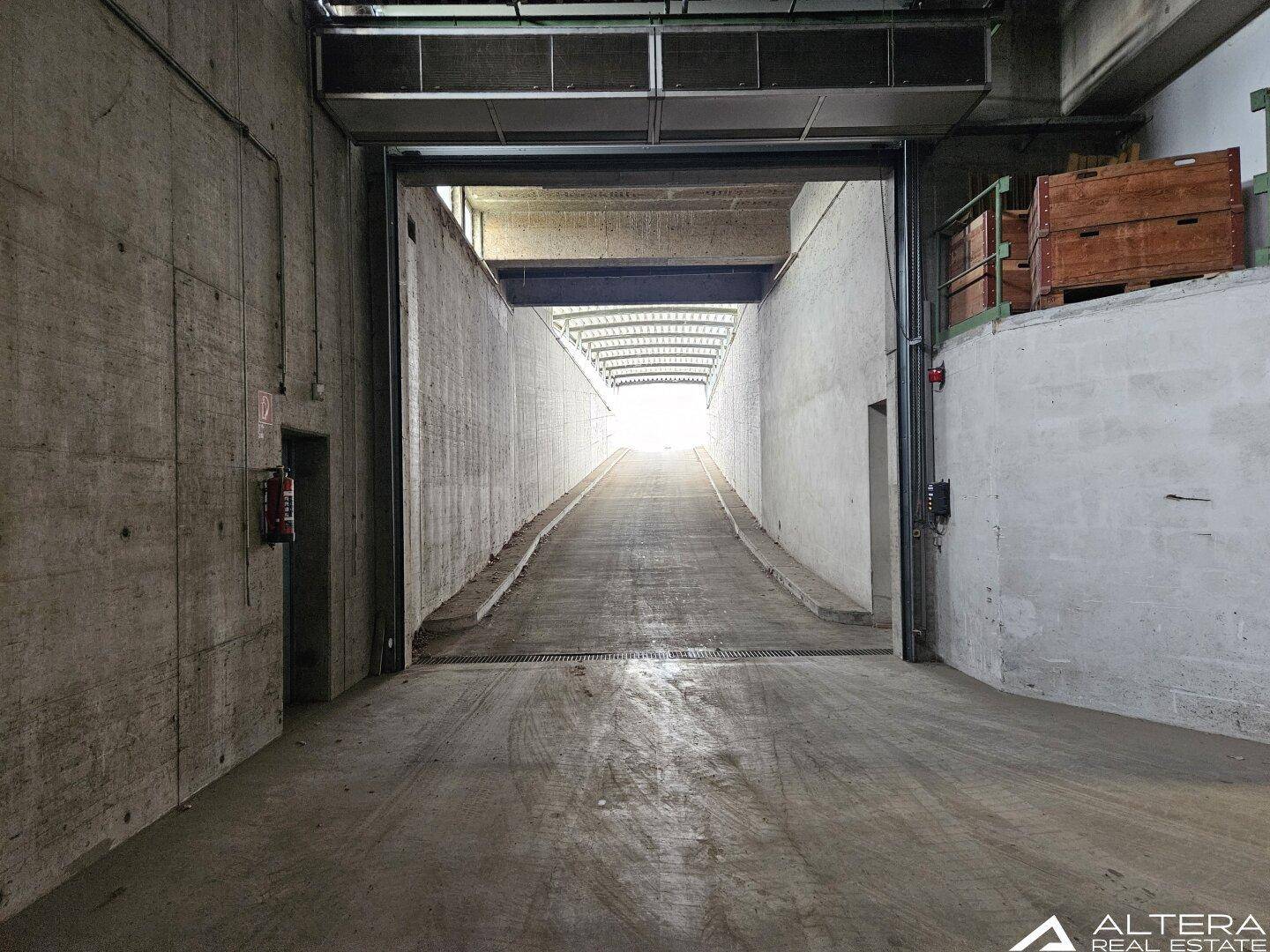 Zufahrtsrampe zu einer Tiefgarage oder Lagerhalle mit Betonwänden und hellem Ausgang.