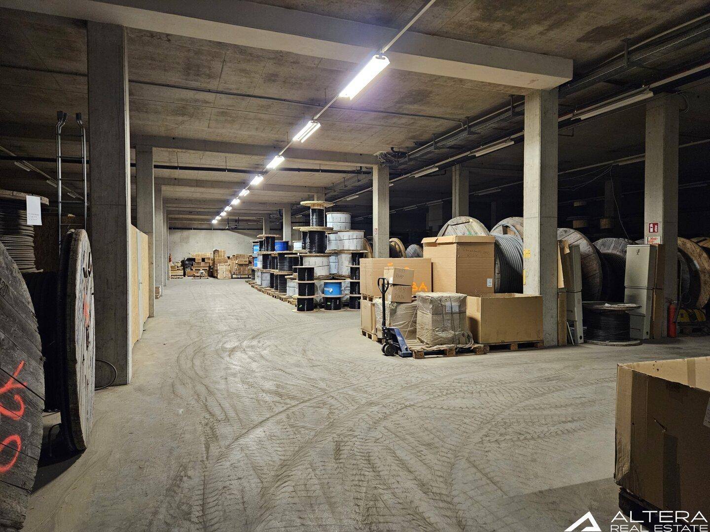 Lagerhalle mit Betonboden, Säulen und Reihen von Kabelrollen und verpackten Waren.