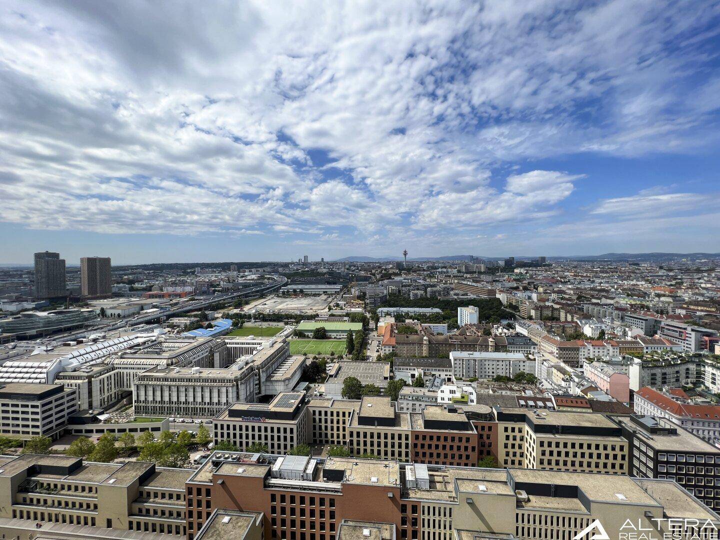 Weitläufiger Panoramablick über die Stadt und ihre grüne Umgebung unter blauem Himmel.