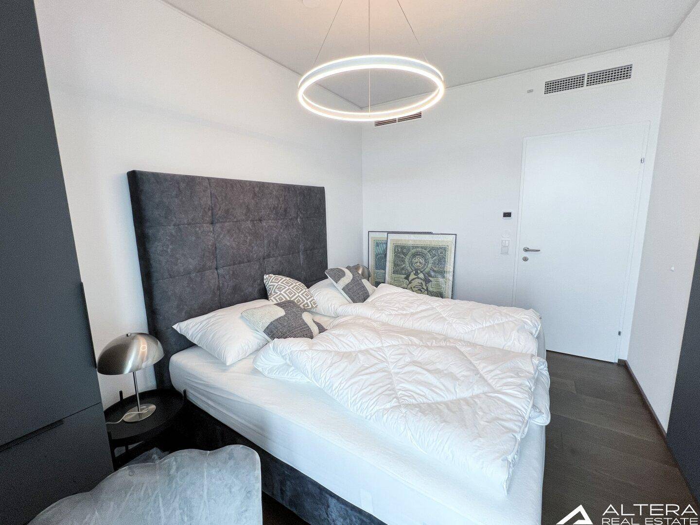 Modernes Schlafzimmer mit gepolstertem Kopfteil und dunklem Holzboden.