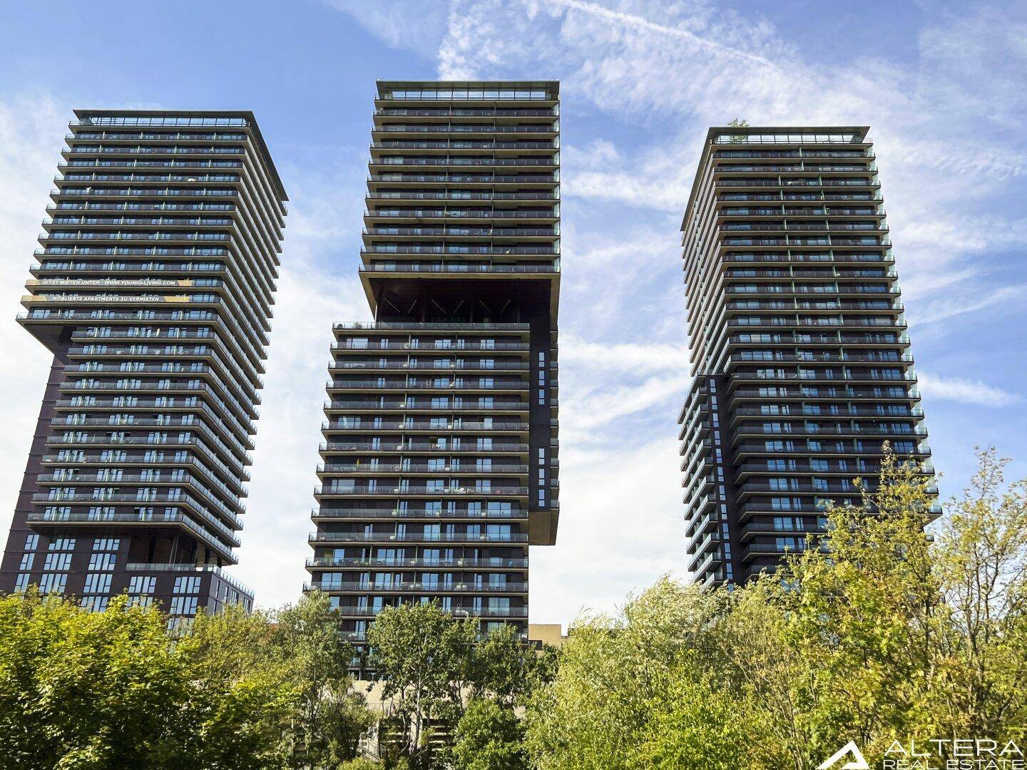 Drei moderne Hochhäuser mit markanter Architektur und vielen Balkonen.