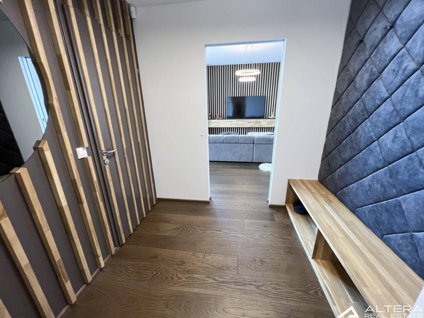 Moderner Flur mit Holzboden und dekorativer Holzlamellenwand, die zum Wohnbereich führt.