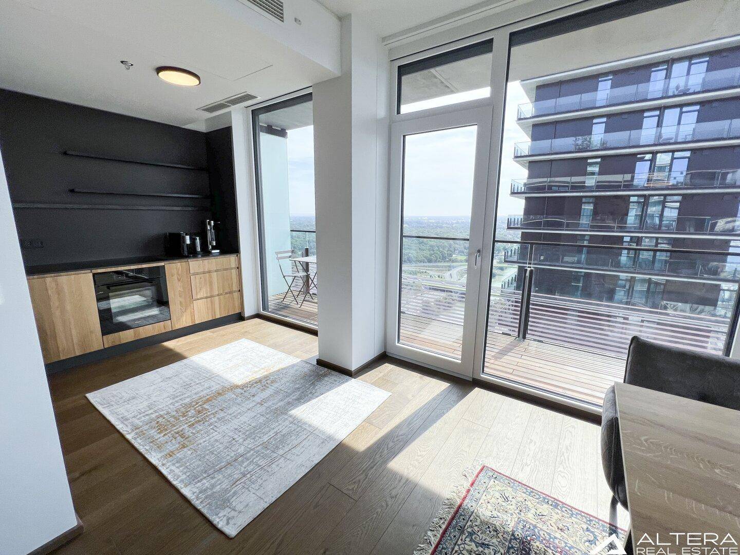 Moderne Küche mit Holzelementen, dunkler Arbeitsplatte und Zugang zum Balkon.