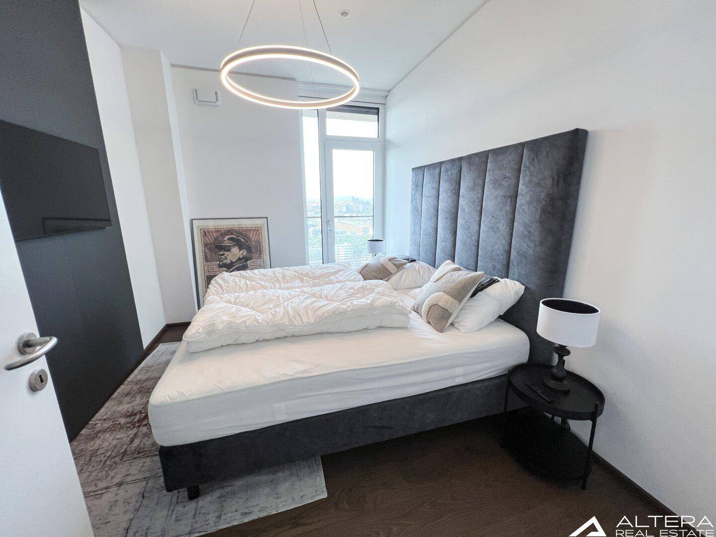Schlafzimmer mit großem Bett, Holzboden und viel Tageslicht durch das Fenster.