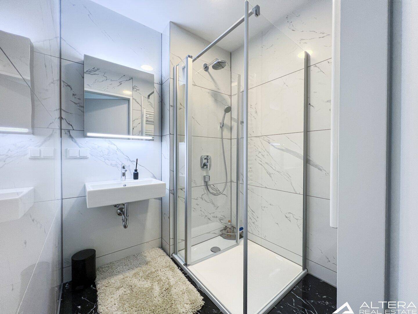 Modernes Badezimmer mit Duschkabine, Einzelwaschbecken und Marmorfliesen.