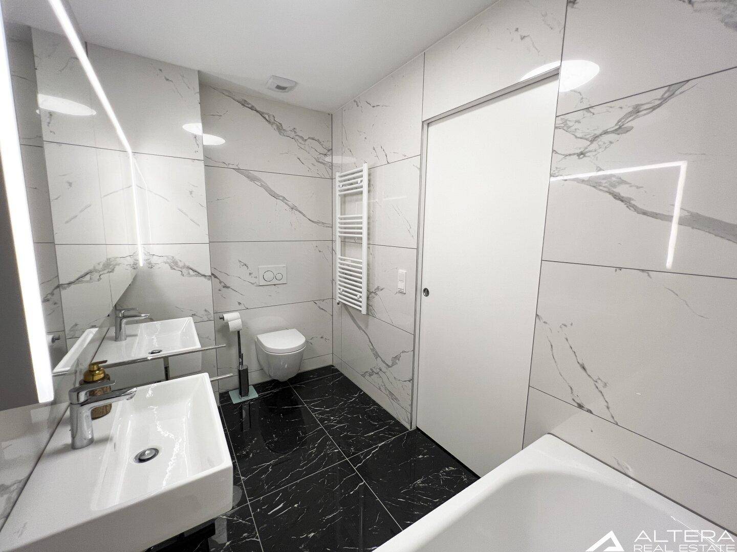 Helles Badezimmer mit Wand-WC, Doppelwaschbecken und stilvollen Marmorfliesen.