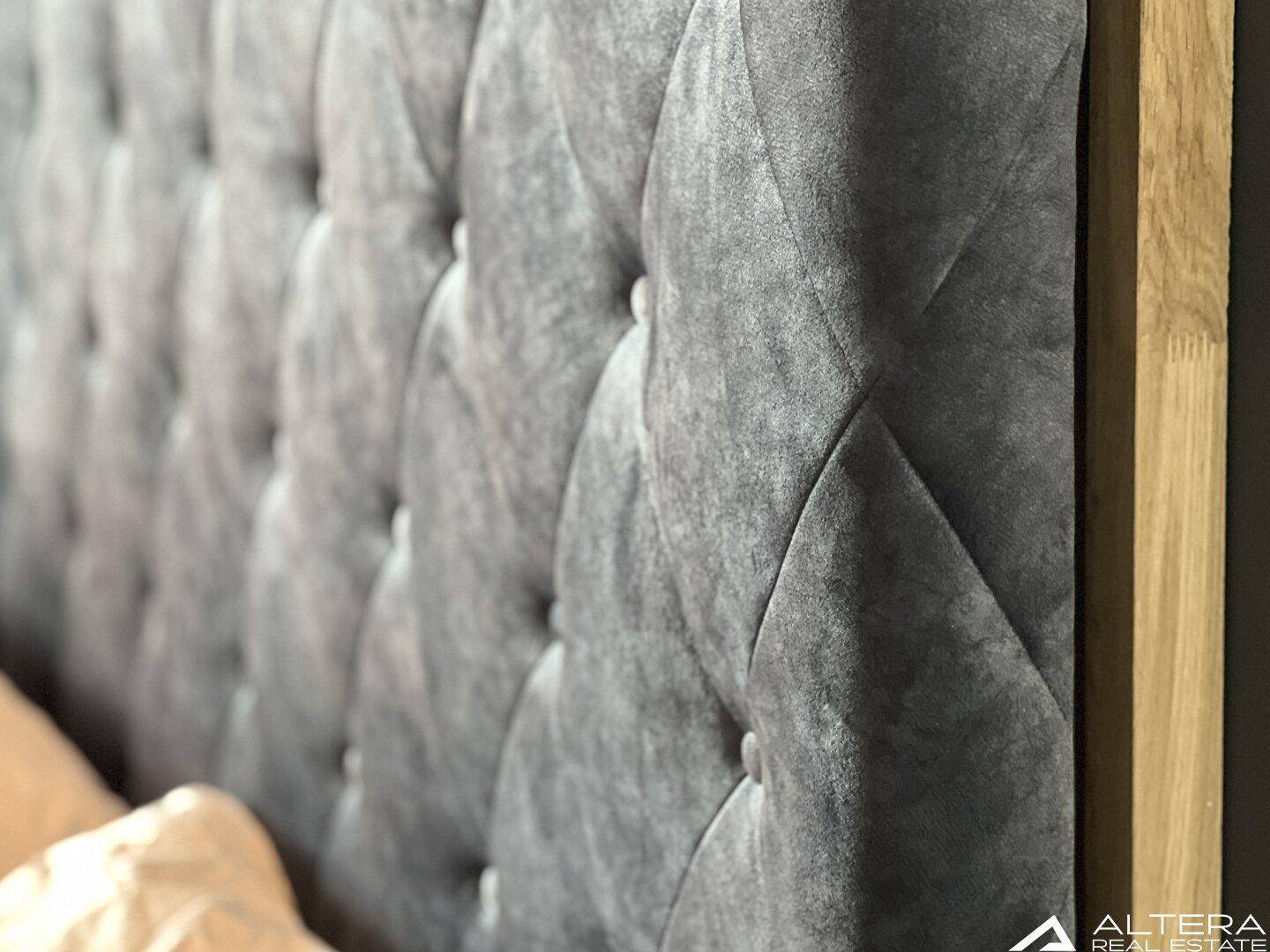 Detailansicht des eleganten, gepolsterten Kopfteils in Grau mit Knopfheftung.
