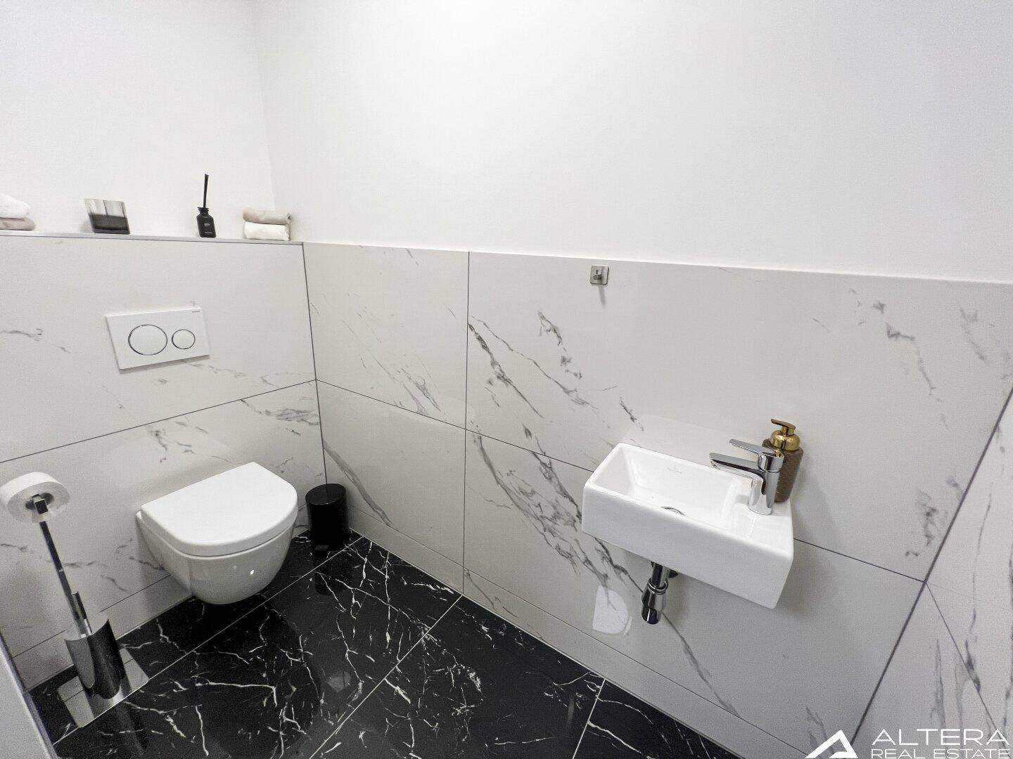 Gäste-WC mit Wand-WC, kleinem Waschbecken und eleganten Marmorfliesen.