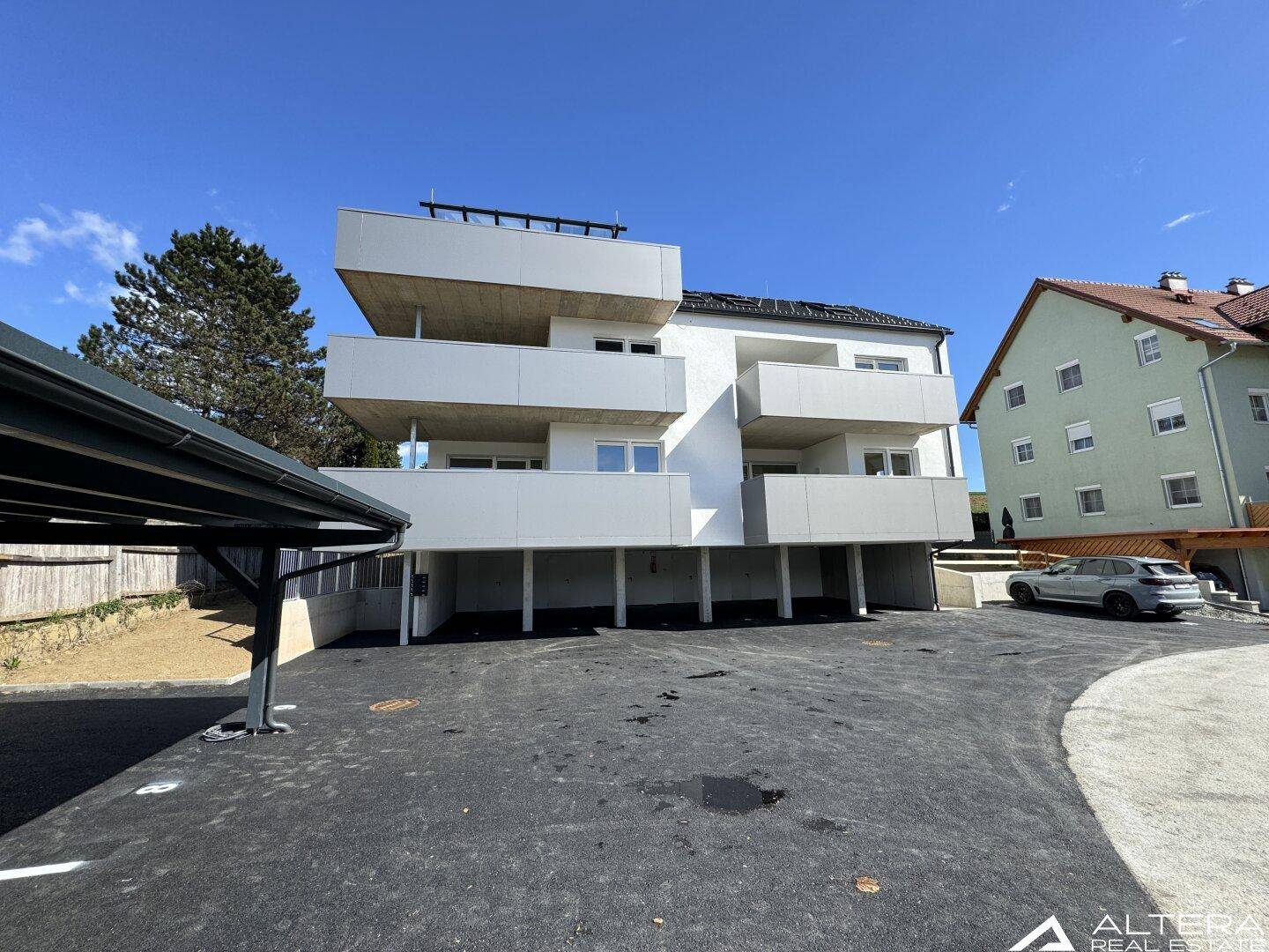 Seitenansicht des modernen Neubaus mit gestuften Balkonen und einem Carport im Vordergrund.