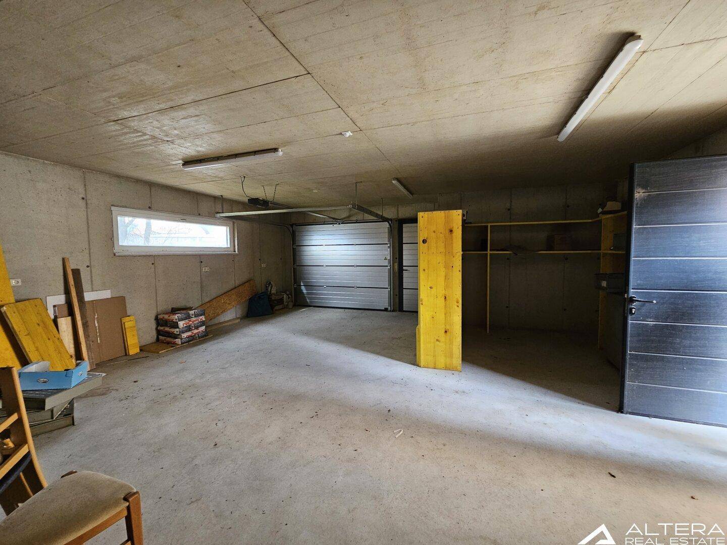 Geräumige Garage mit Betonboden, Rolltor und einem Fenster, ideal als Werkstatt.