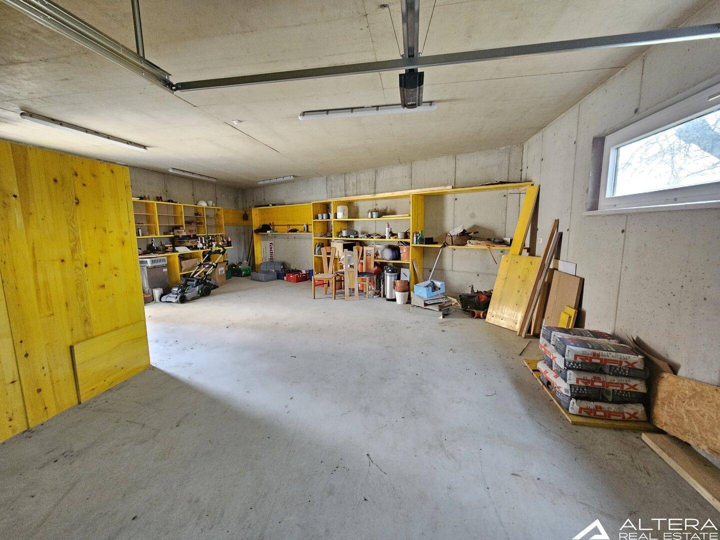 Große Garage mit Betonboden, gelben Regalen und viel Stauraum für Werkzeuge und Geräte.