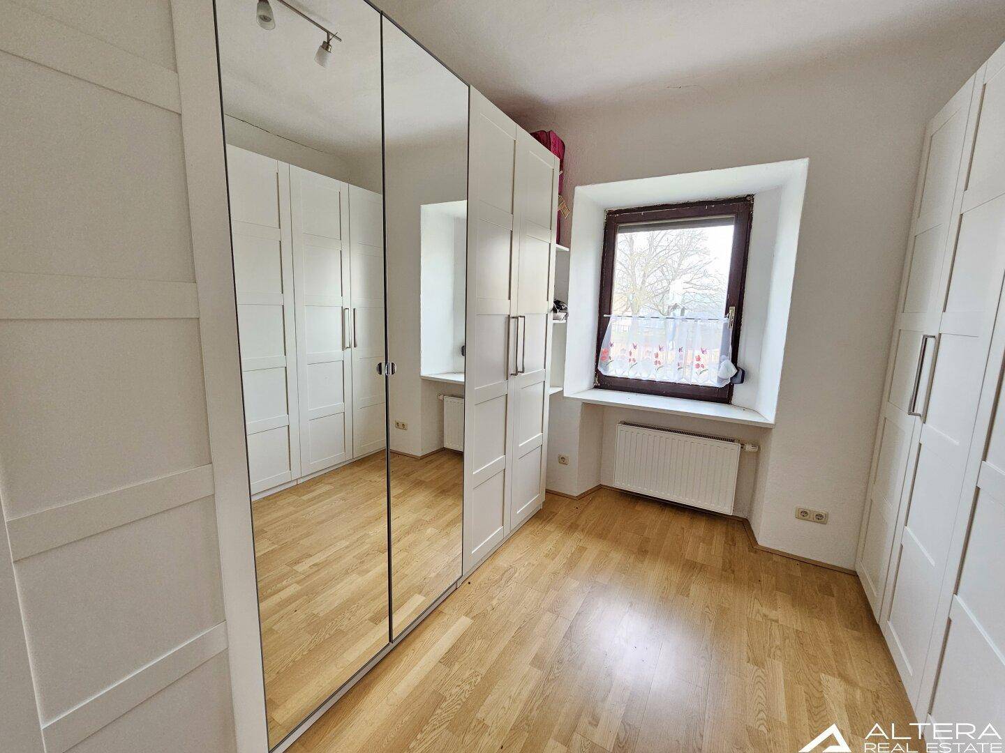 Schlafzimmer oder Ankleidezimmer mit Holzparkett, weißen Schränken und einem Fenster.