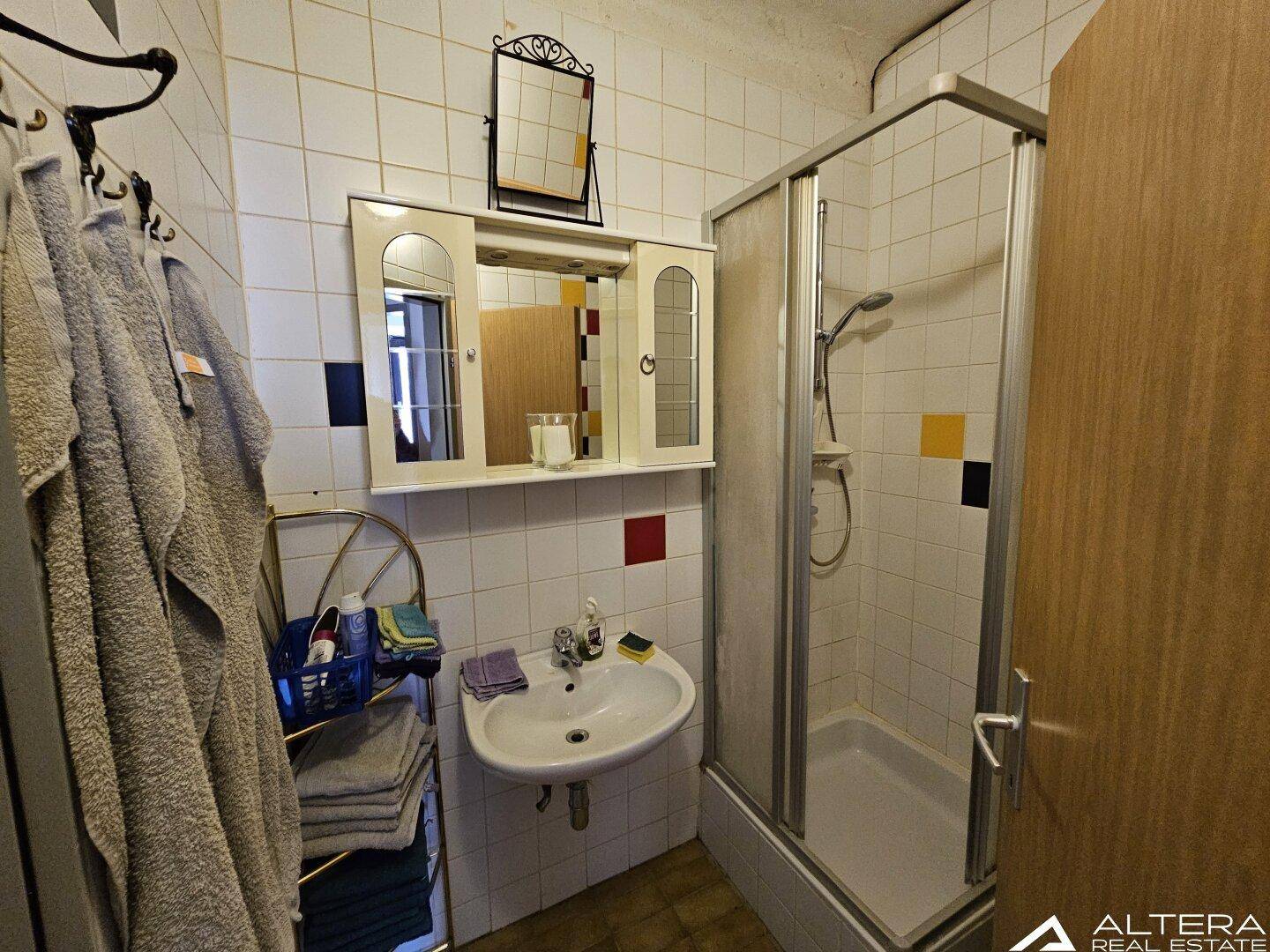 Badezimmer mit Duschkabine, Waschbecken und Fliesen in verschiedenen Farben.