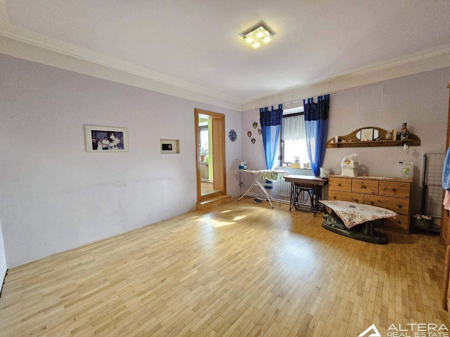 Geräumiges Zimmer mit Holzparkettboden, blauen Vorhängen und einem Fenster, vielseitig nutzbar.