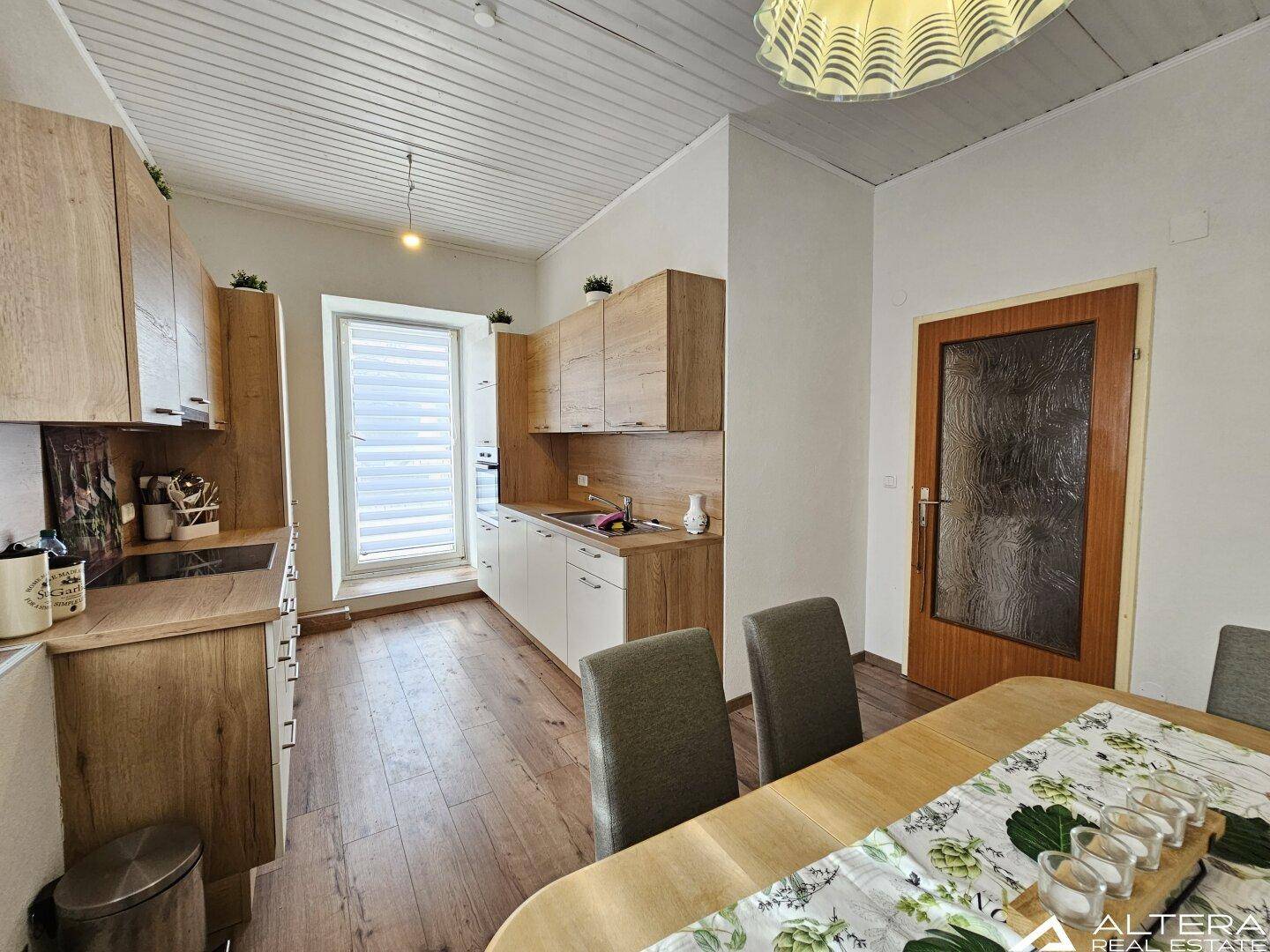 Helle Küche mit Holzboden, modernen Schränken und einem Esstisch, mit Zugang zu einem Fenster.