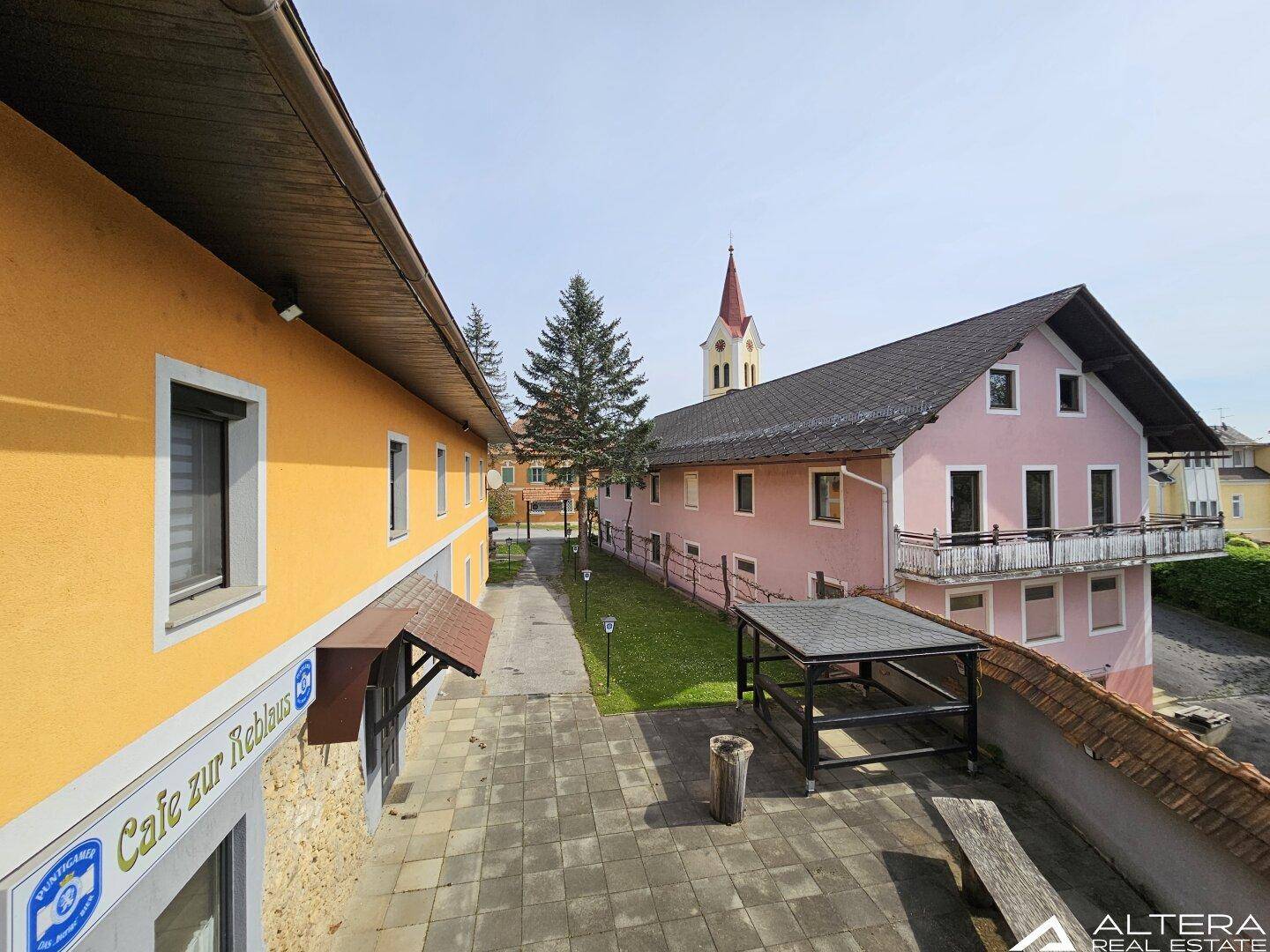 Panoramablick auf den gepflasterten Innenhof, das rosa Gebäude mit Balkon und die nahegelegene Kirche.
