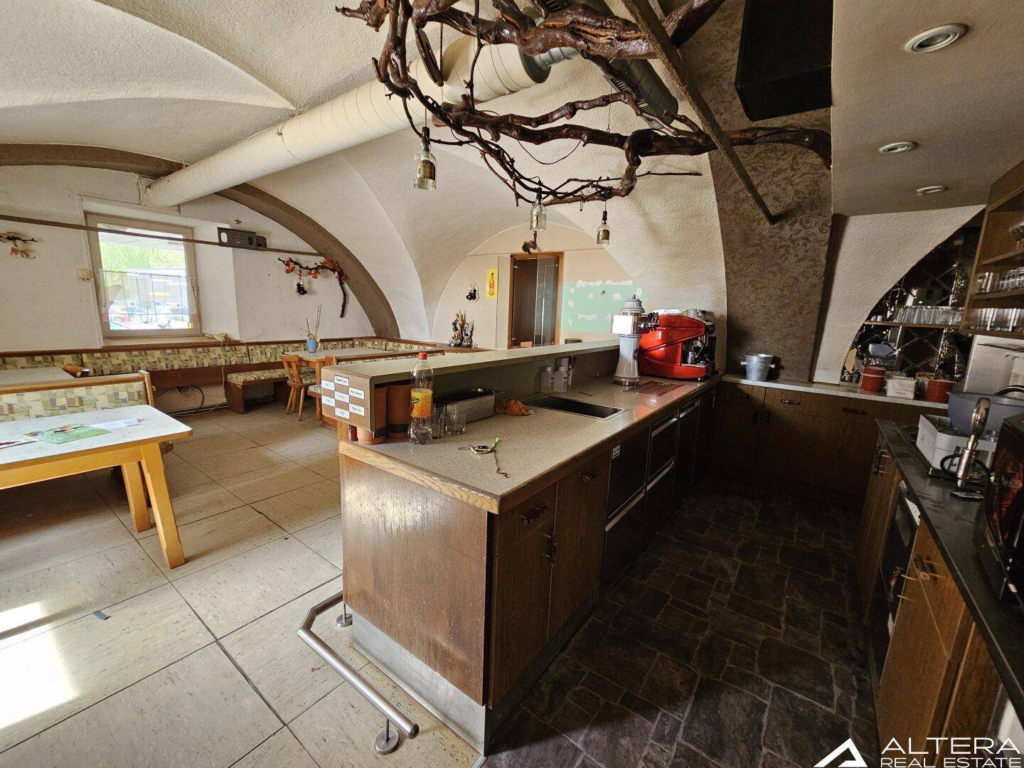 Bar- und Sitzbereich mit Gewölbedecke, rustikalen Holzelementen und Fliesenboden.