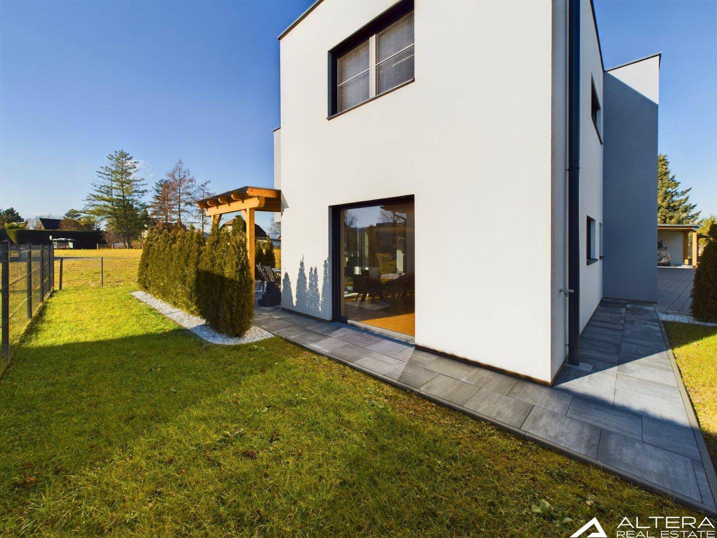 Moderne Hausfassade mit großen Fenstern und Zugang zum Gartenbereich auf der Seite des Hauses.
