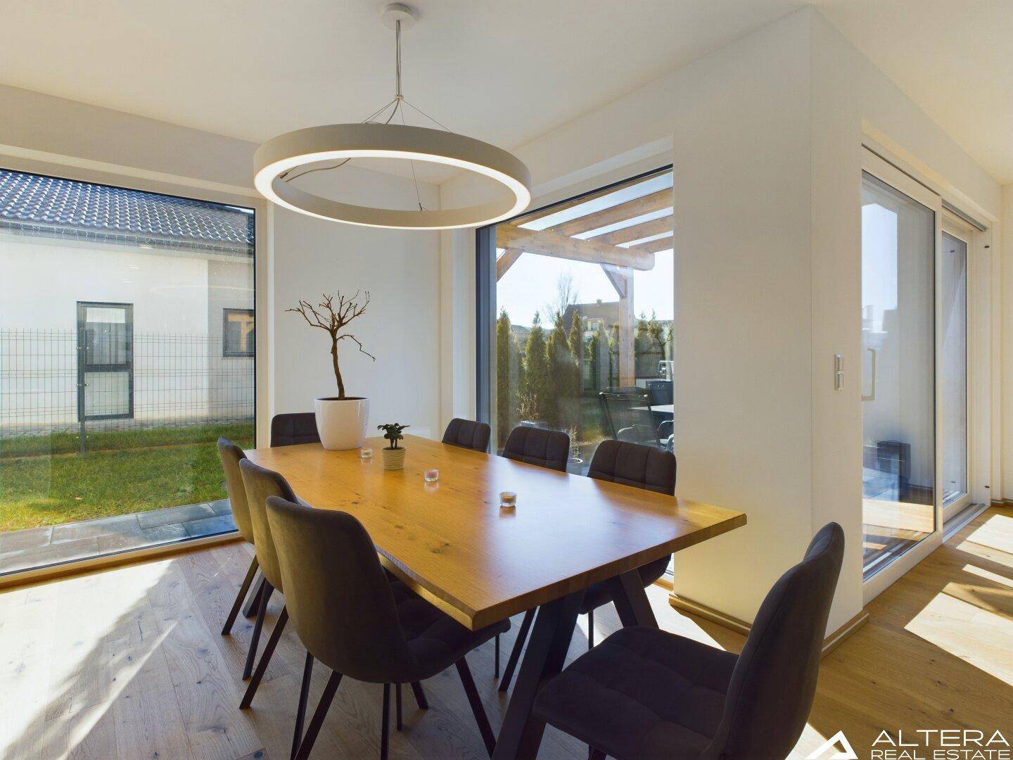 Lichtdurchfluteter Essbereich mit Holztisch, modernen Stühlen und raumhohen Fenstern.