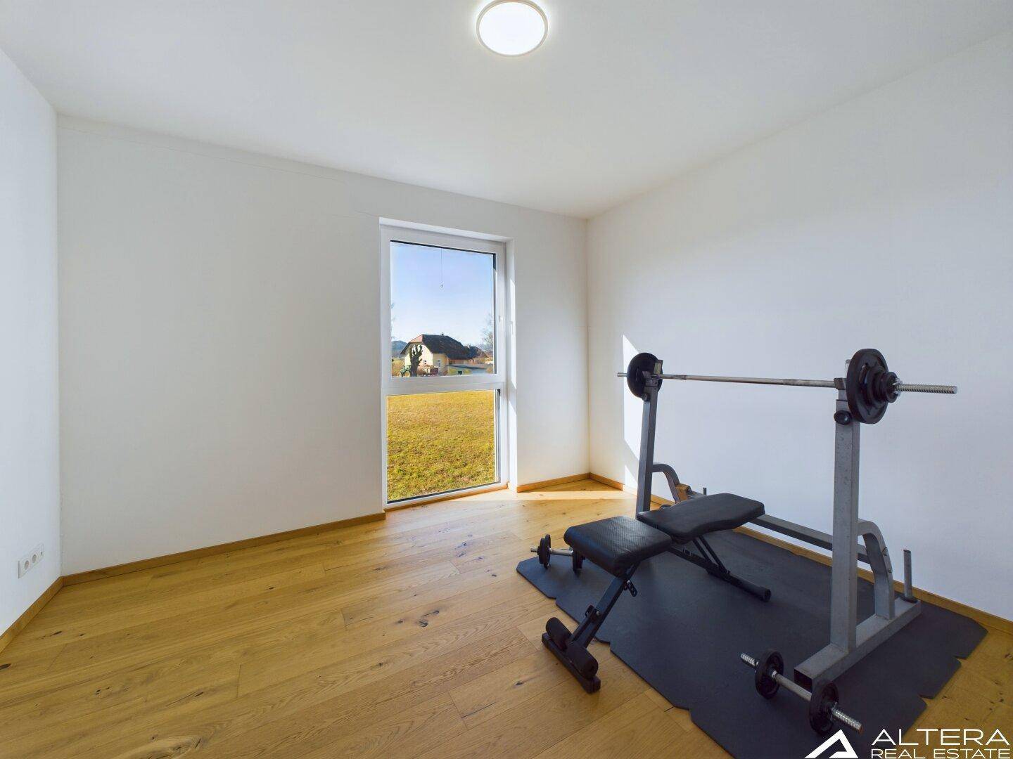Raum eingerichtet als Fitnessbereich mit Hantelbank und Holzboden, ideal für Sport zu Hause.