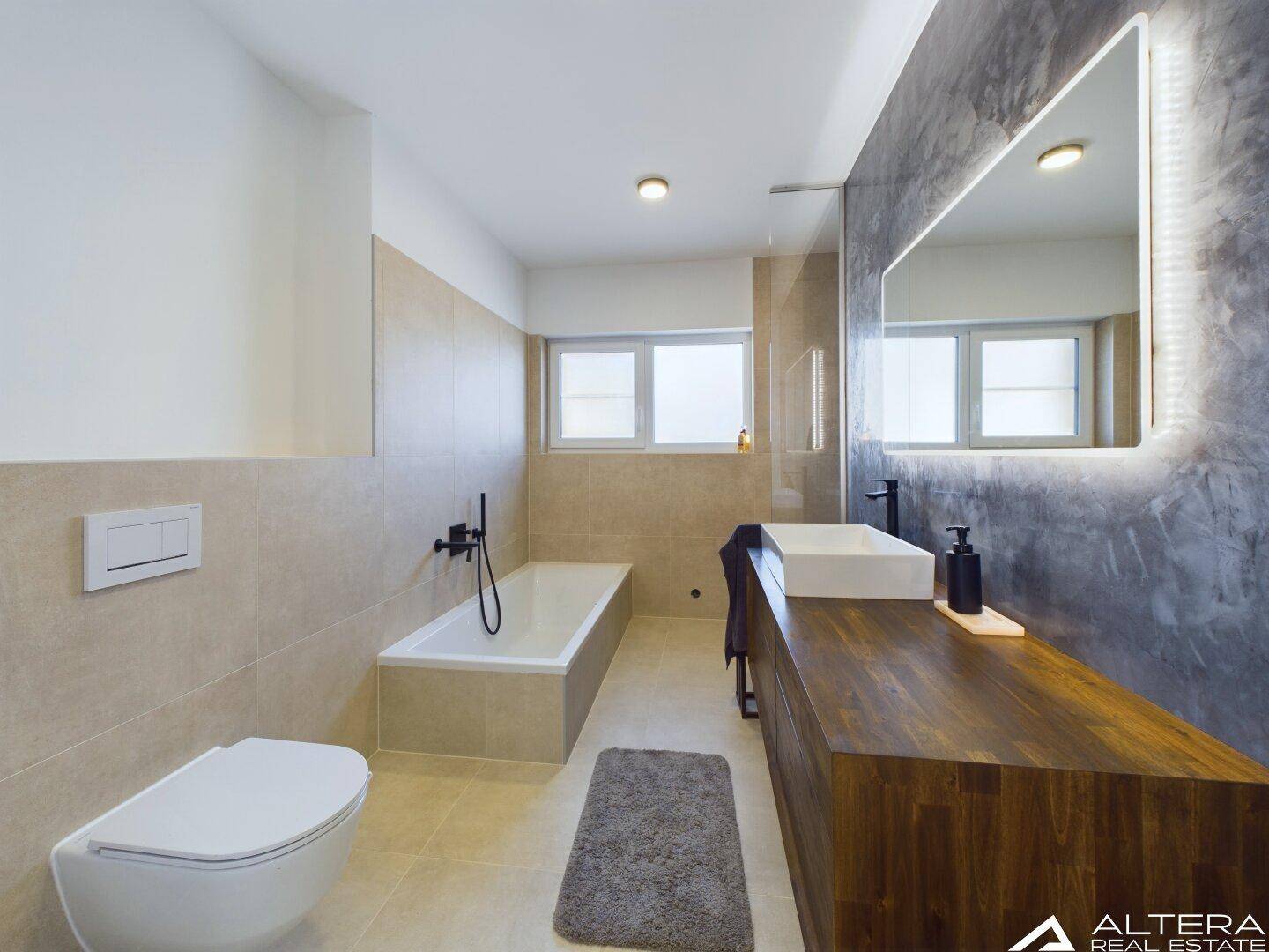 Modernes Badezimmer mit Badewanne, Waschtisch und einem großen, beleuchteten Spiegel.