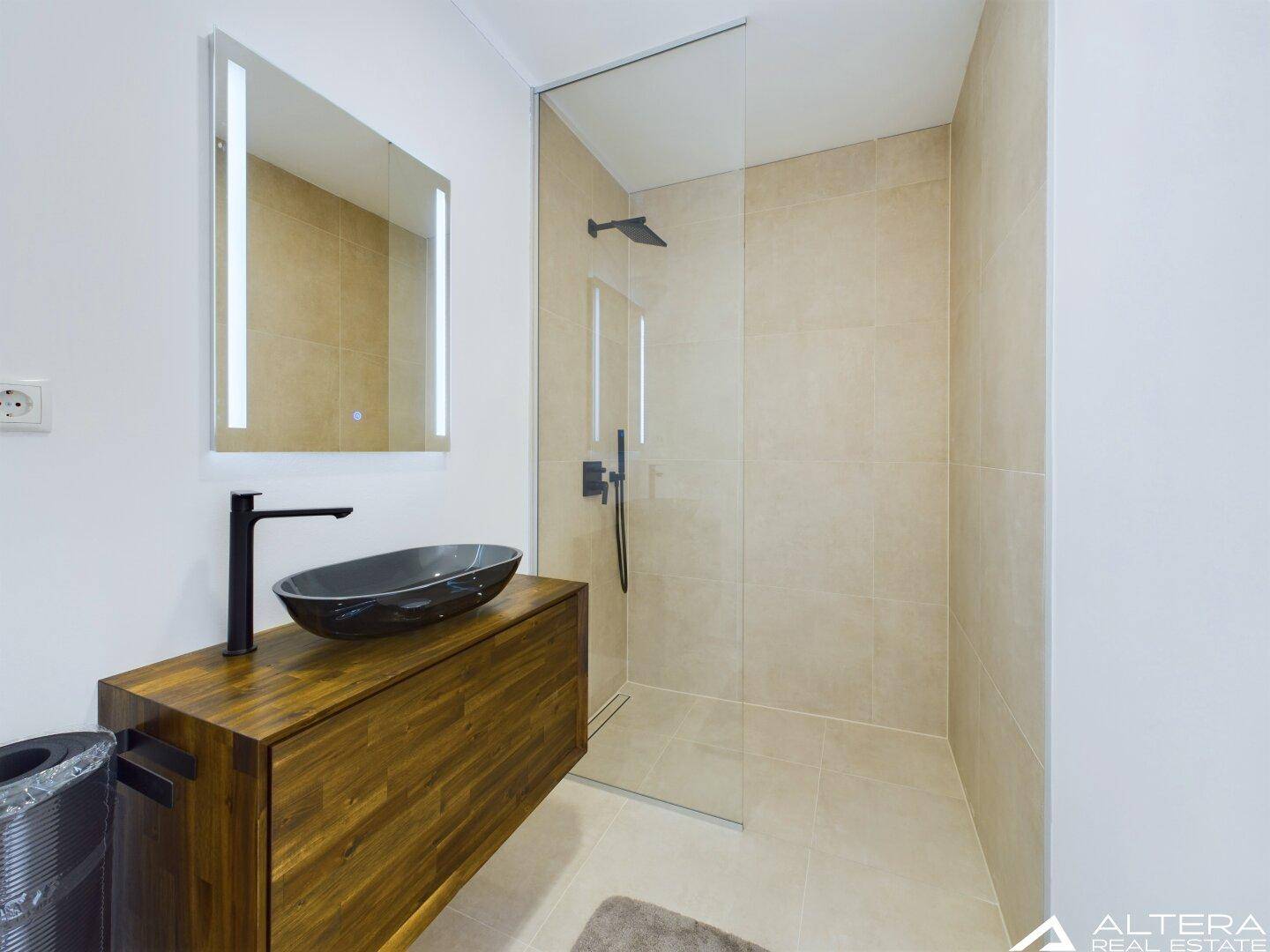 Modernes Badezimmer mit ebenerdiger Dusche, Waschtisch und einem beleuchteten Spiegel.